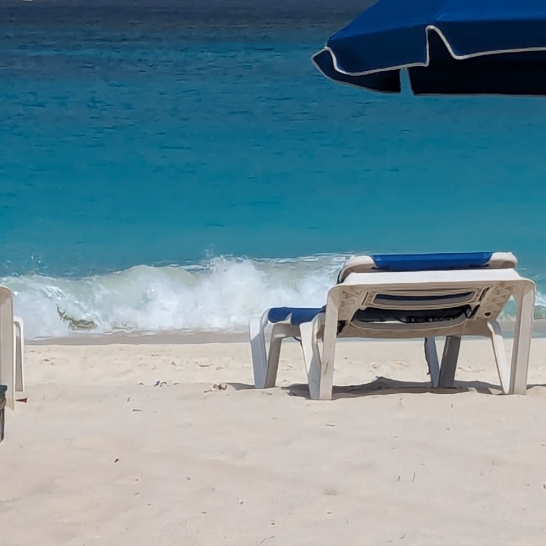 Lounge chair under umbrella on the beach with rough waves